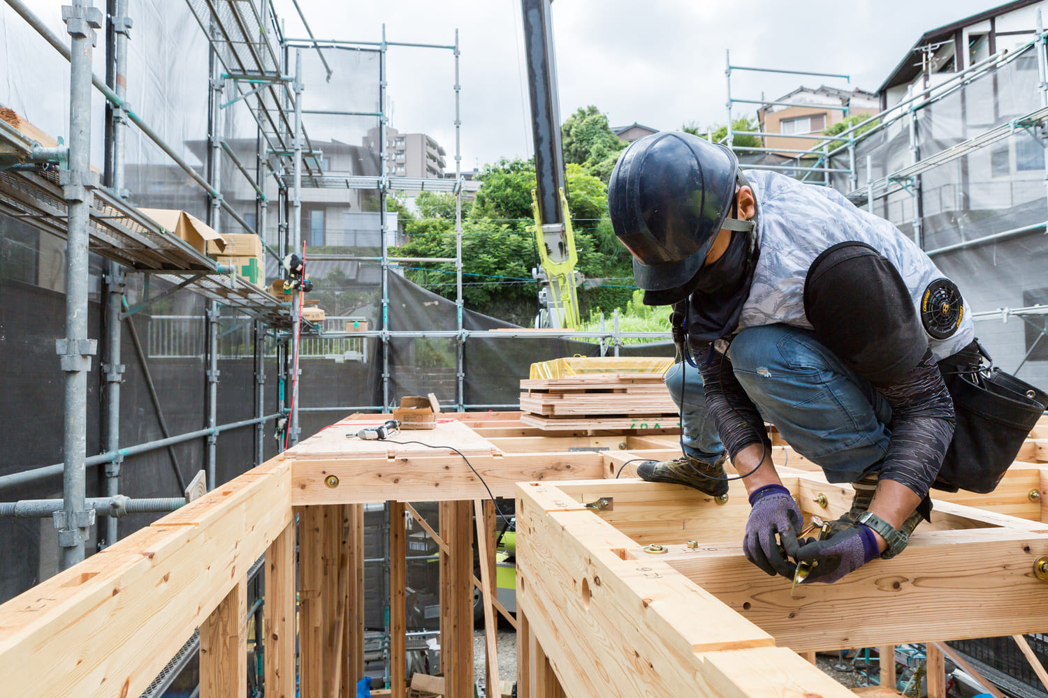 家の骨組みの上にのり、建築作業を行う作業着姿の男性の写真